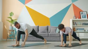 Woman and man are working out at home doing yoga together synchronously on mats caring for body health. Modern people, sports and apartment concept.